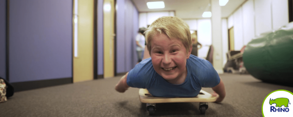 Boy rolls down a corridor on a body roller in a sensory integration session.