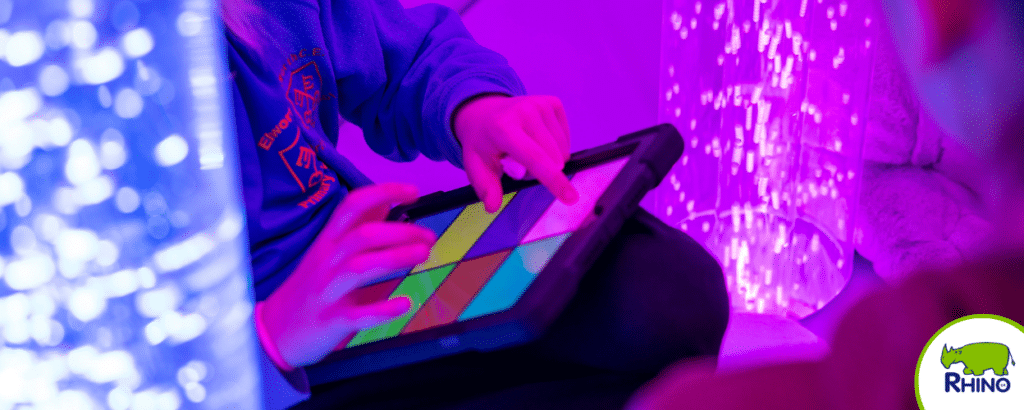 A person relaxes in a sensory room, choosing the colours of the bubble tubes from an ipad.
