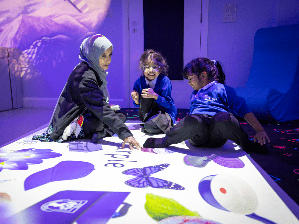 A teacher and two students sit and interactive with the Rhino Wonderfloor