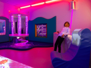 Girl leans back against the ball pool, stood next to a sensory rocker chair.