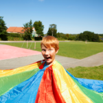 Boy popping his head out of the middle of a parachute and pulling a silly face