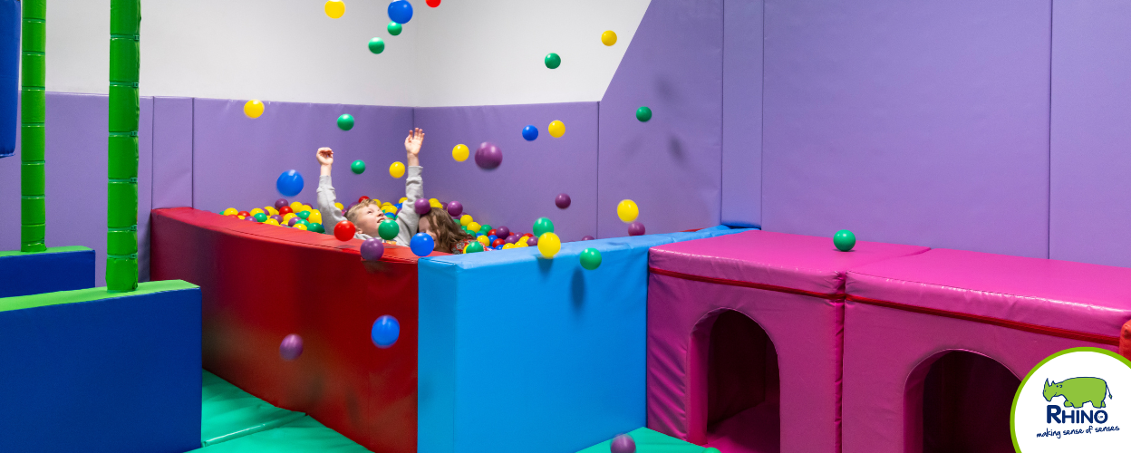 A child throws ball pool balls up into the air inside a soft play room.